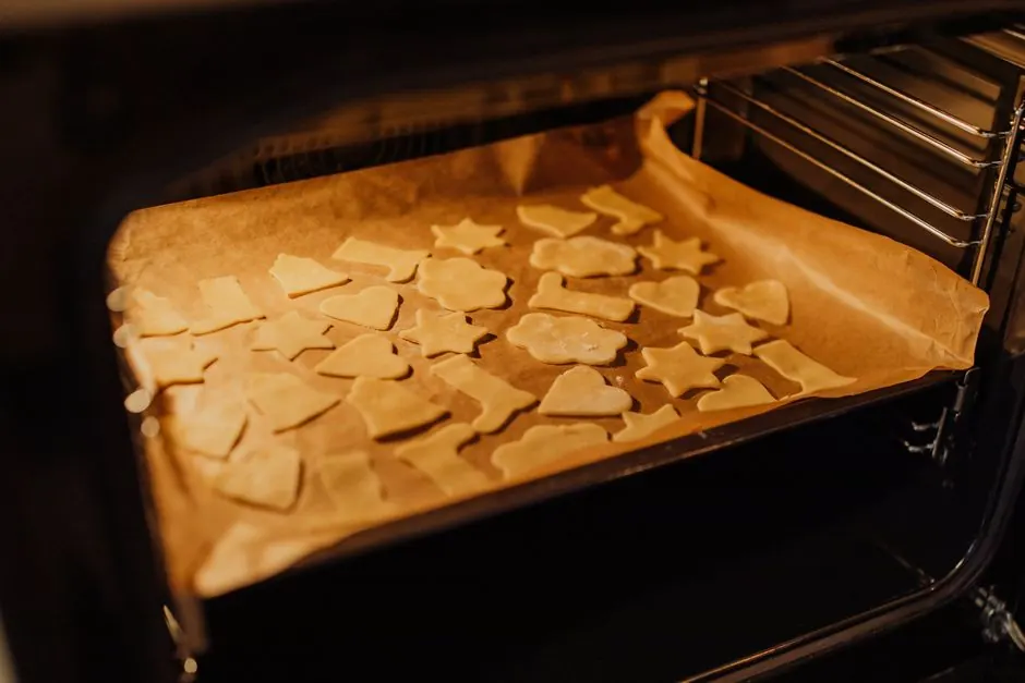 Tray of unbaked Christmas cookies shaped like stars and hearts in an oven.